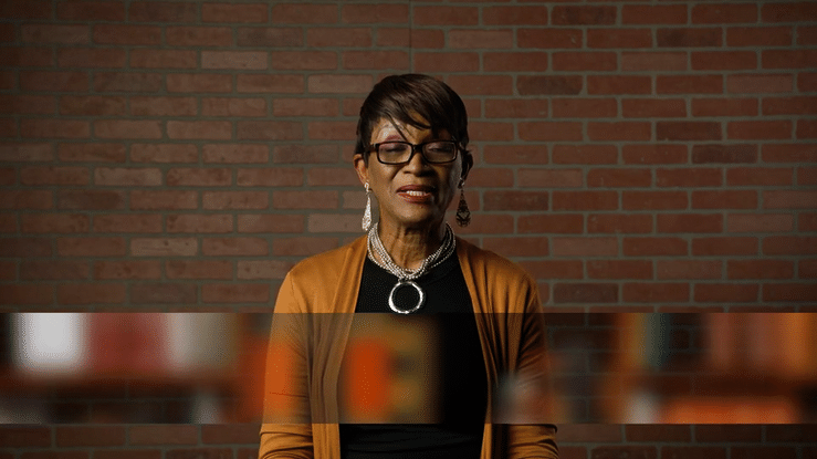 Video of older black women wearing orange cardigan with black dress shirt asking Dr. Michael Heiser "Who wrote the Bible?'